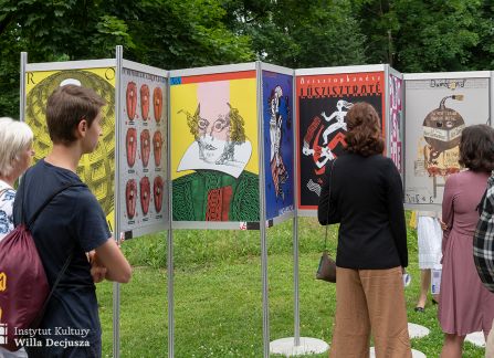 fotografia. art piknik w willi decjusza. plenerowa wystawa plakatów teatralnych. grupa ludzi przed ustawionymi w rzędzie plakatami.